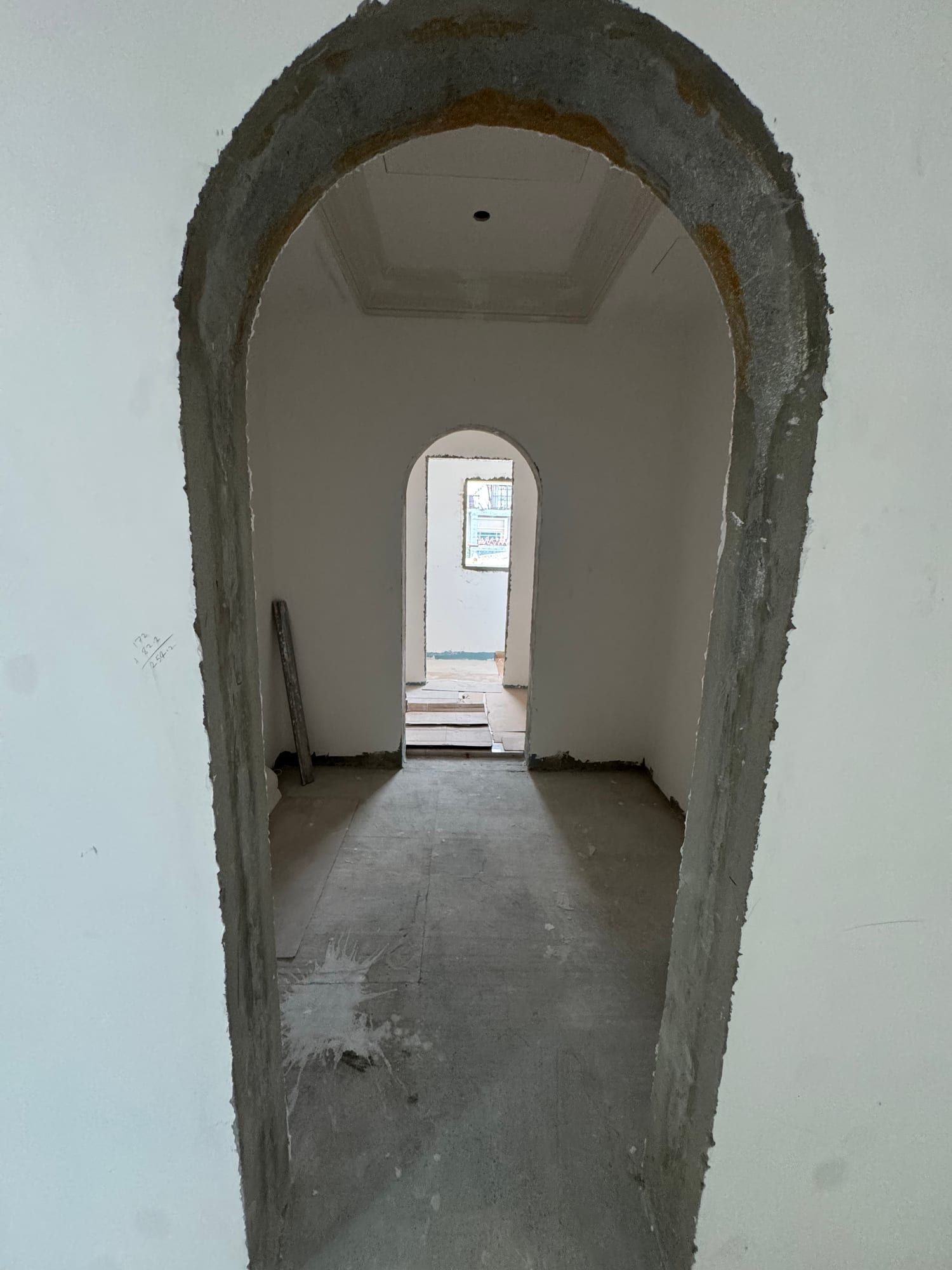 Arched opening with a raw plaster edge, looking through two rooms to a smaller arch beyond